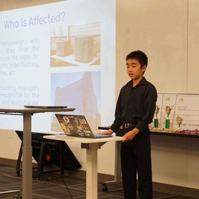 Competitor presenting a Who is Affected poster to the room