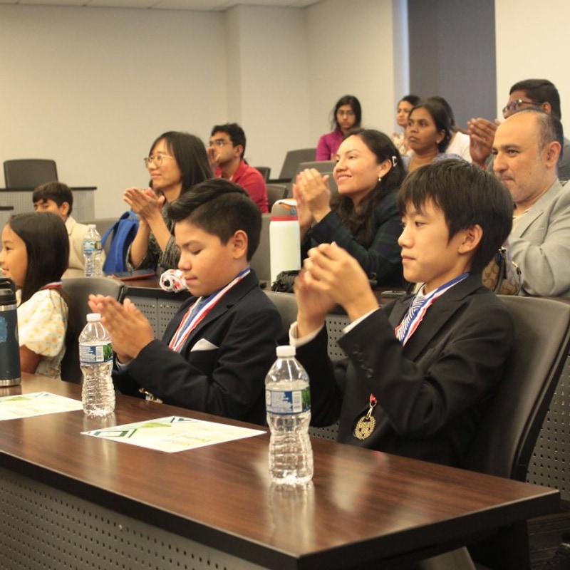 Two boys in suits with medals clapping in the lecture hall audience