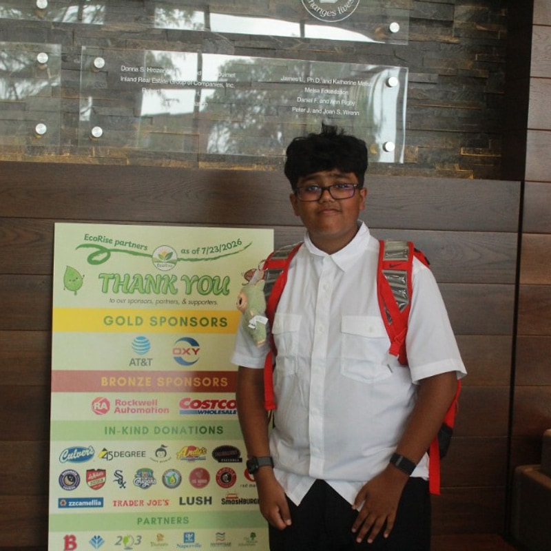 Teen with glasses posing by the Green Dream sponsor board