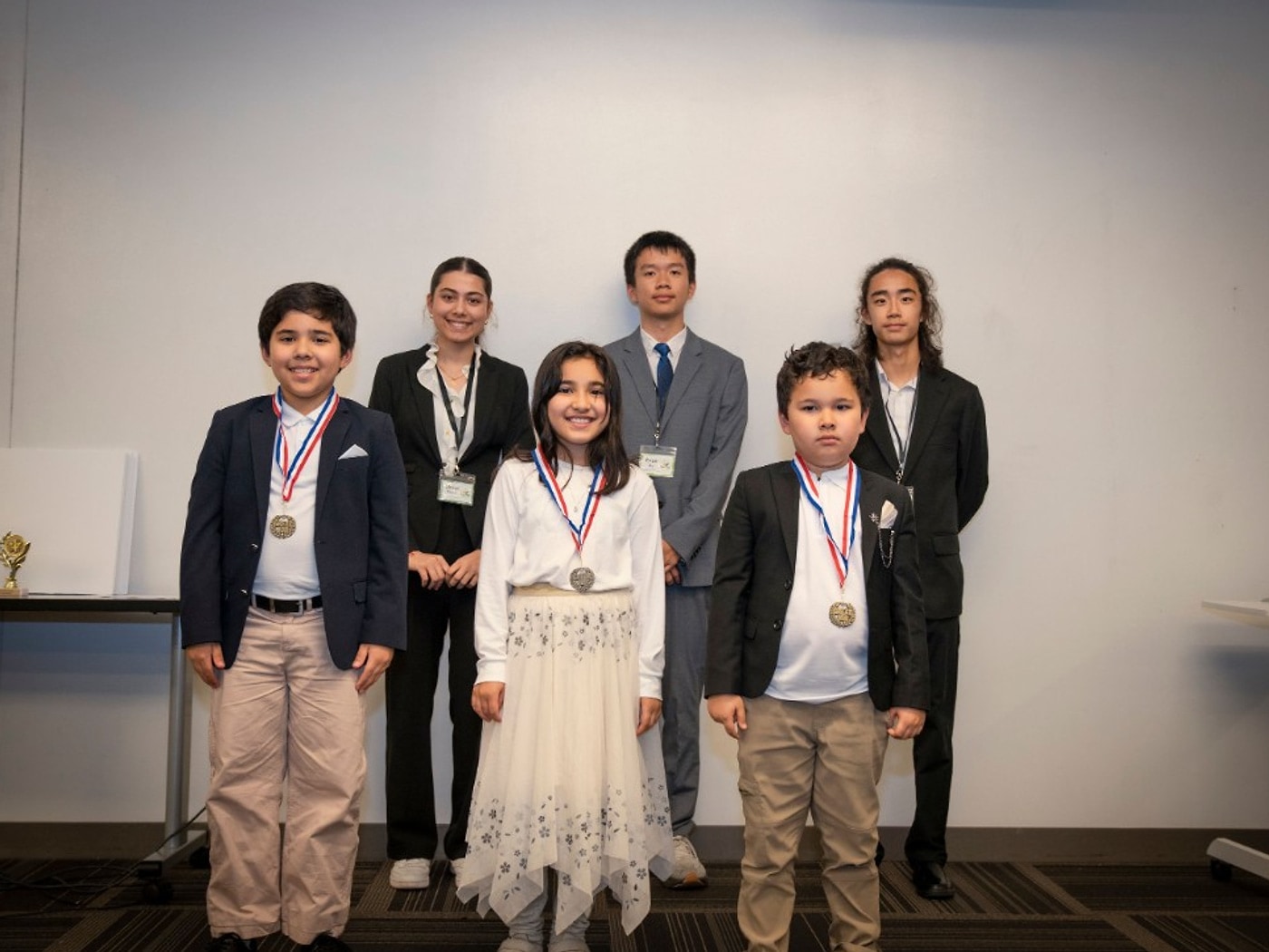 Abdurahman Yuldash, Soleha Yuldash, and Abdullah Yuldash with medals for BuzBomb sixth place, with mentors standing behind