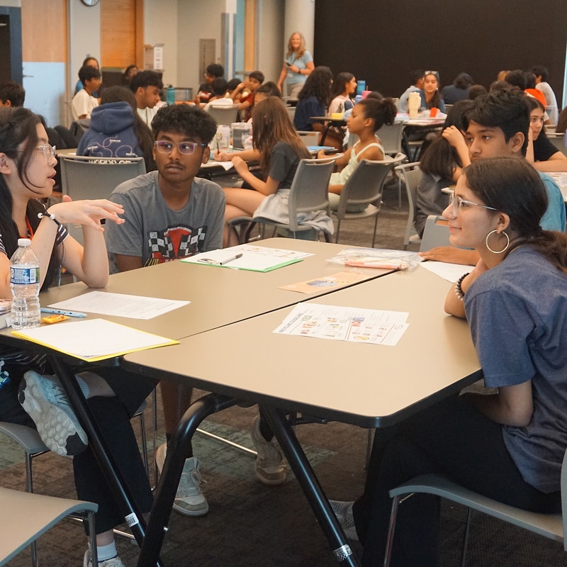EcoRise teens collaborating at a workshop table, student in a striped shirt gesturing