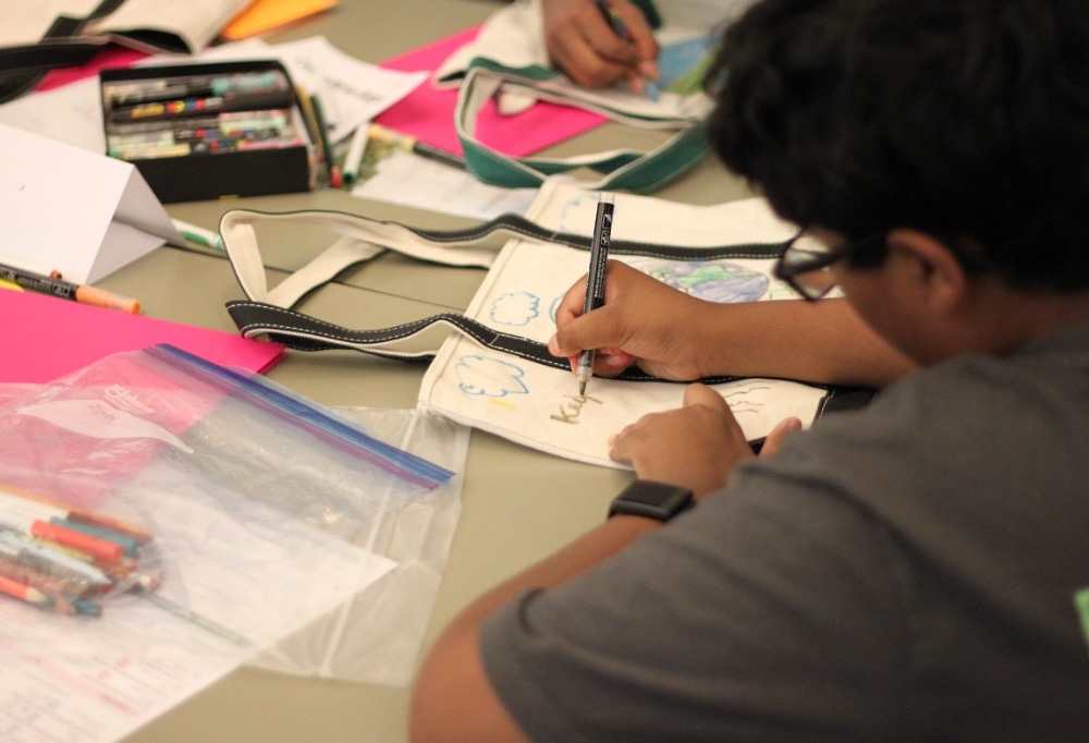 Student decorating a reusable tote bag with sustainability artwork
