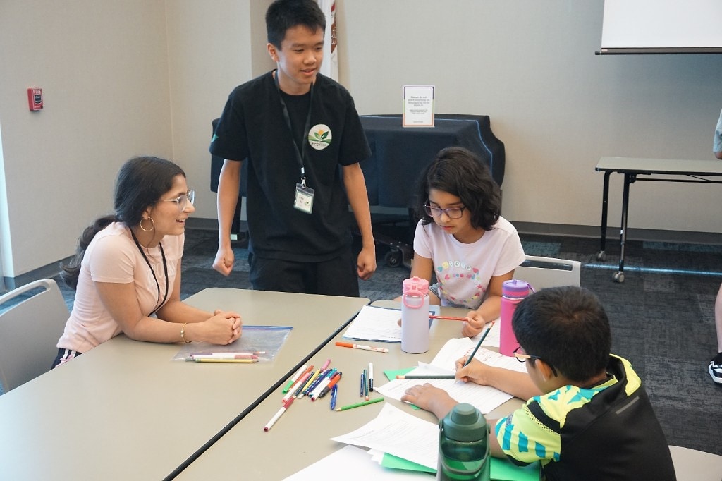 EcoRise camp mentor working with students at a workshop table